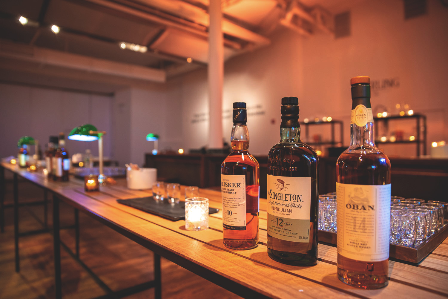 Bottles of whiskey and glasses on a tasting table with ambient lighting in the background.