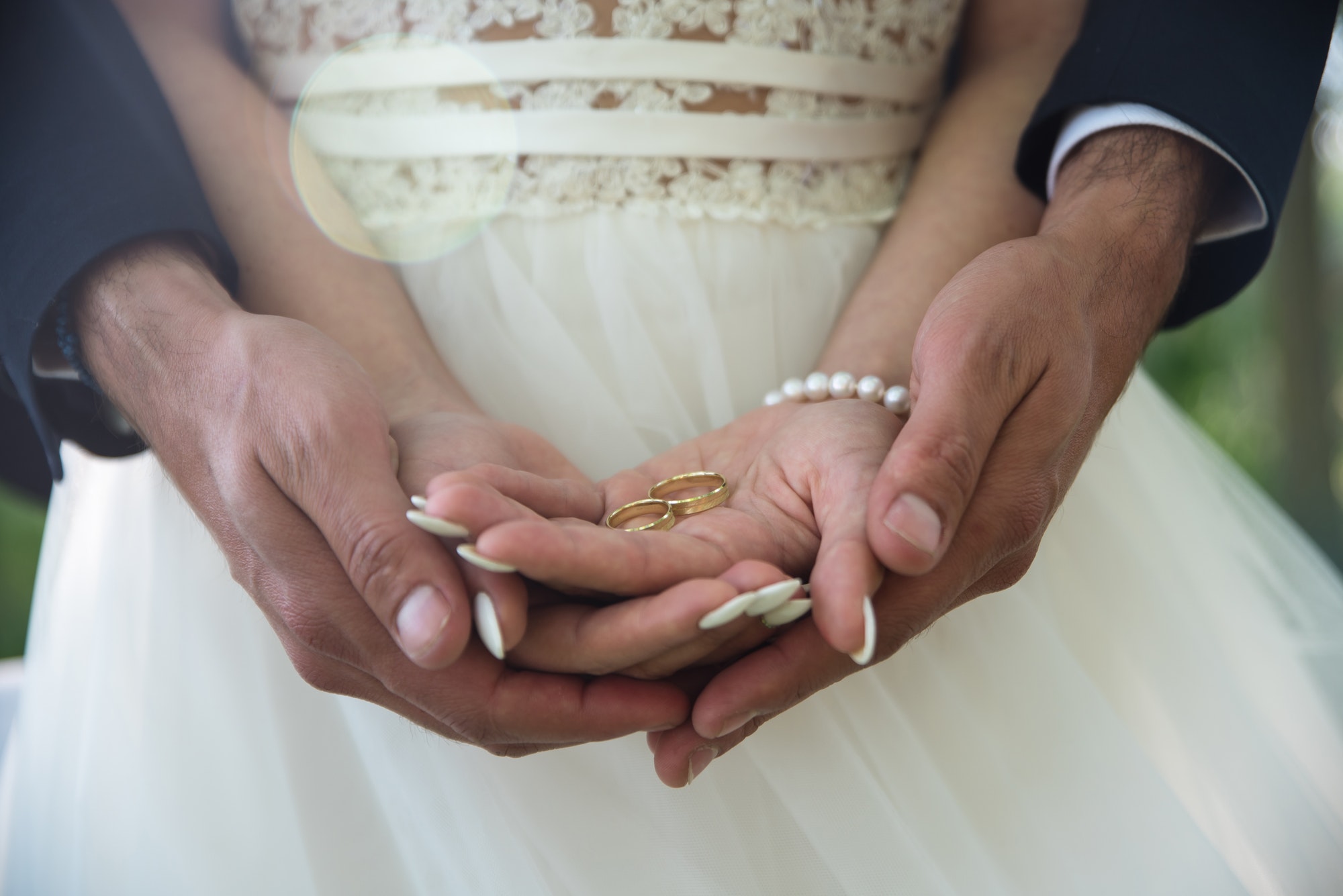 A bride and groom holding hands, displaying wedding rings.