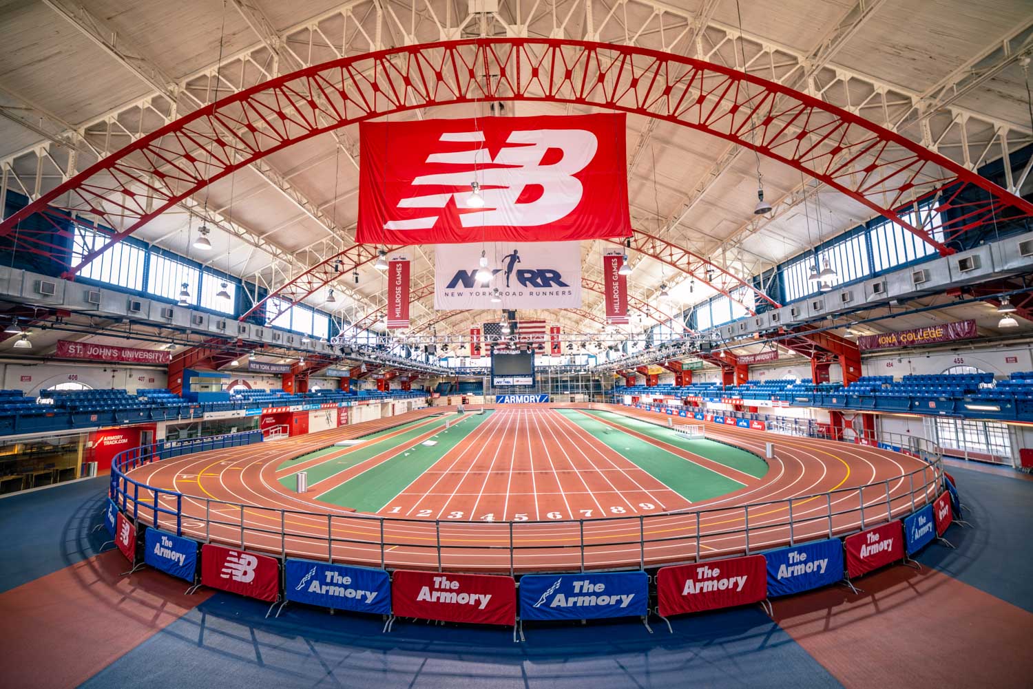 Indoor athletic facility featuring an oval running track with seating areas and a large hanging banner displaying a new balance logo.