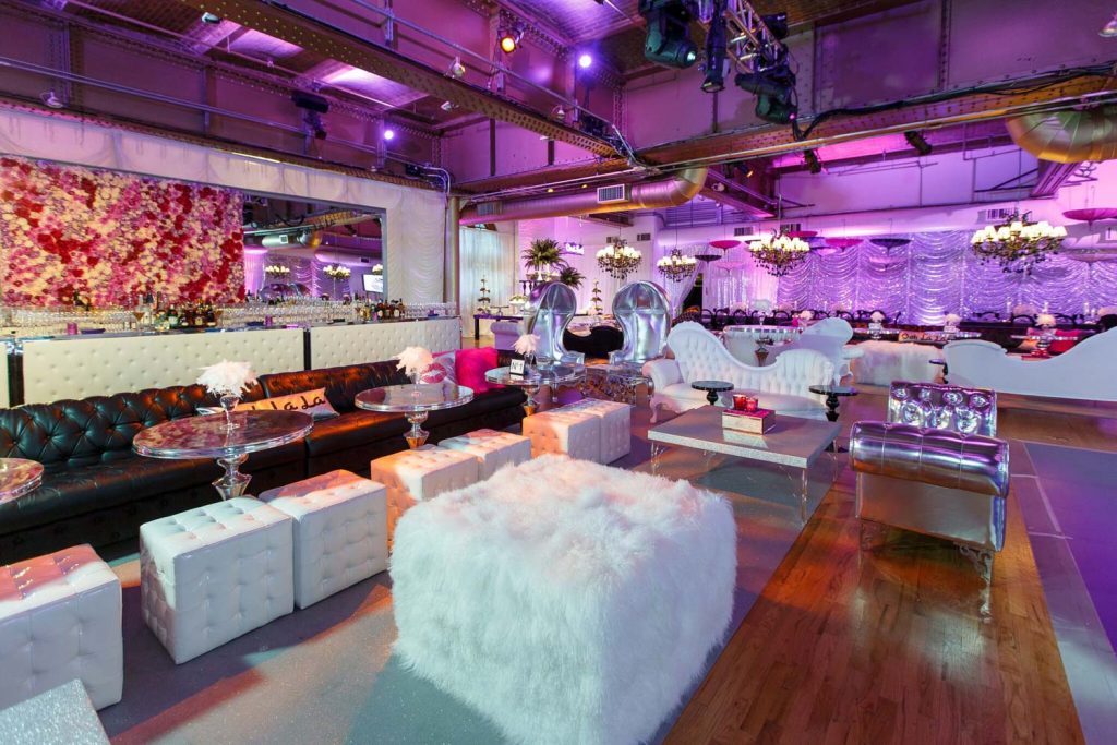 A vibrant event space with eclectic furniture, colorful lighting, and a floral wall backdrop.