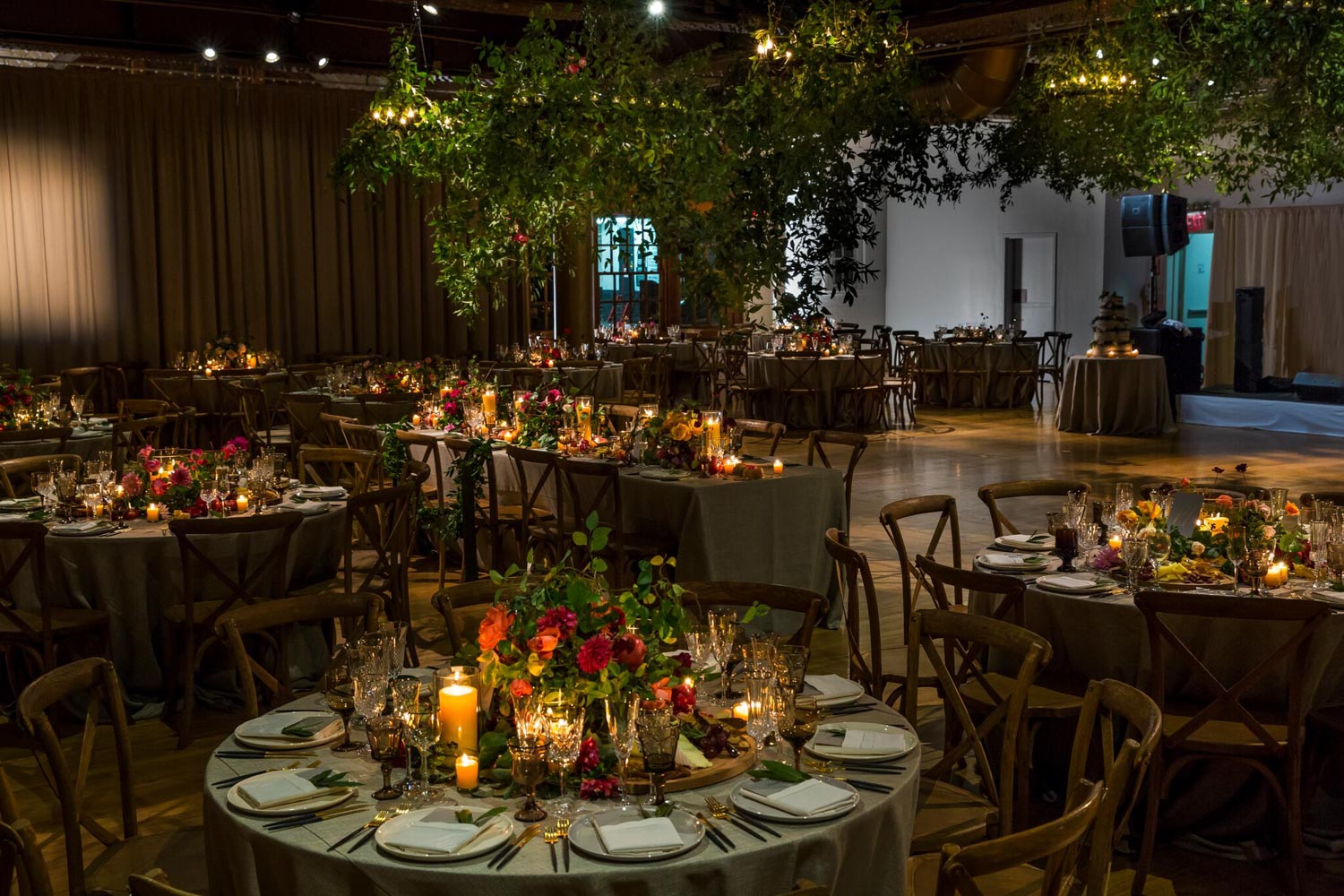 Elegant banquet hall setup with round tables, floral centerpieces, lit candles, and folded napkins, awaiting guests.