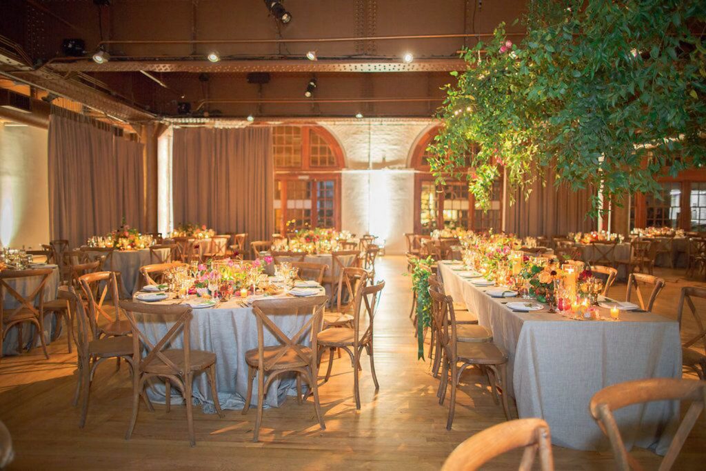 Elegantly set tables for a banquet in a room with warm ambient lighting and decorative indoor trees.