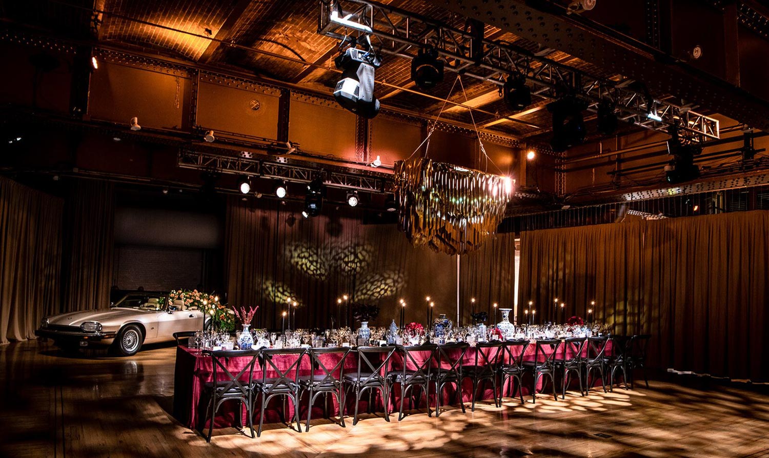 Elegant banquet table set for a sophisticated event with vintage car on display in a grand hall.