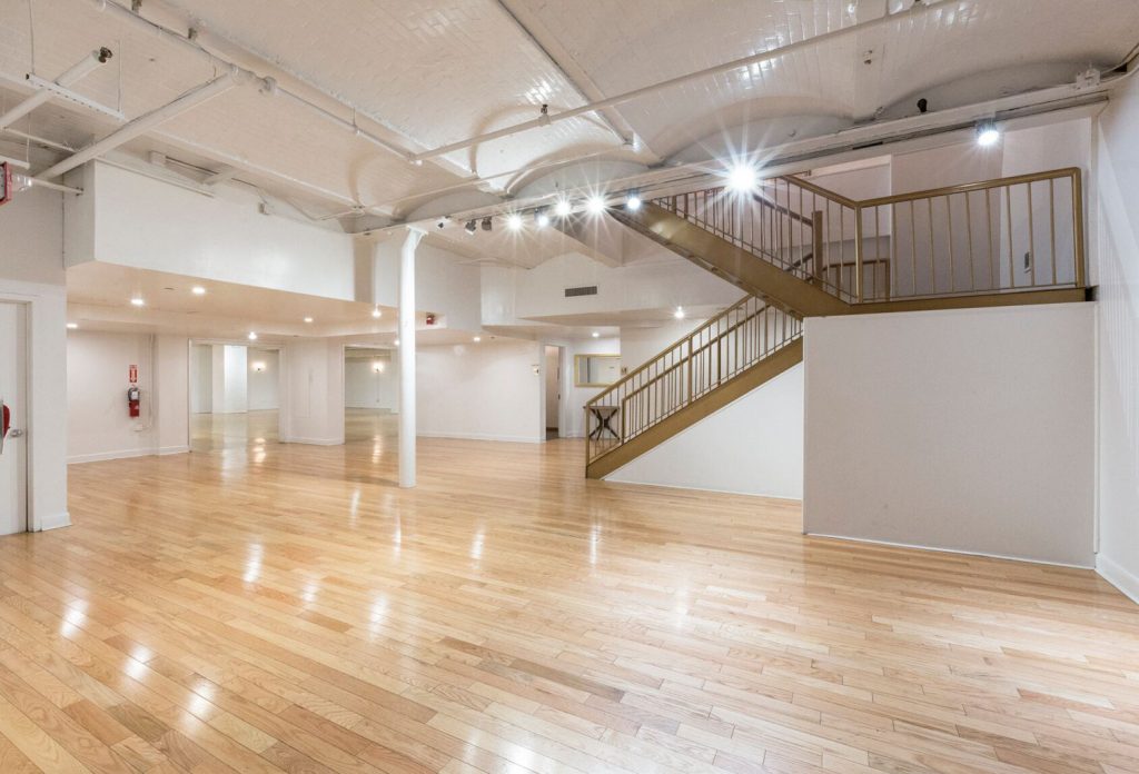 Spacious interior of a modern gallery with wooden floors and a staircase leading to a mezzanine.