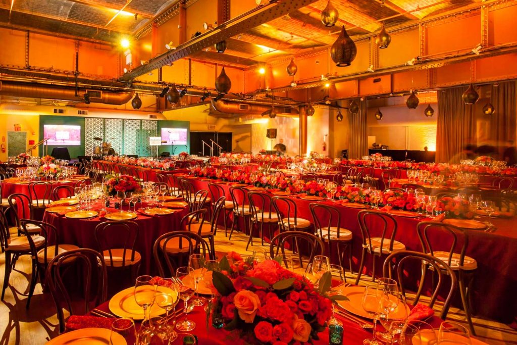 Elegantly set tables for a formal event in a warmly lit banquet hall with floral centerpieces.