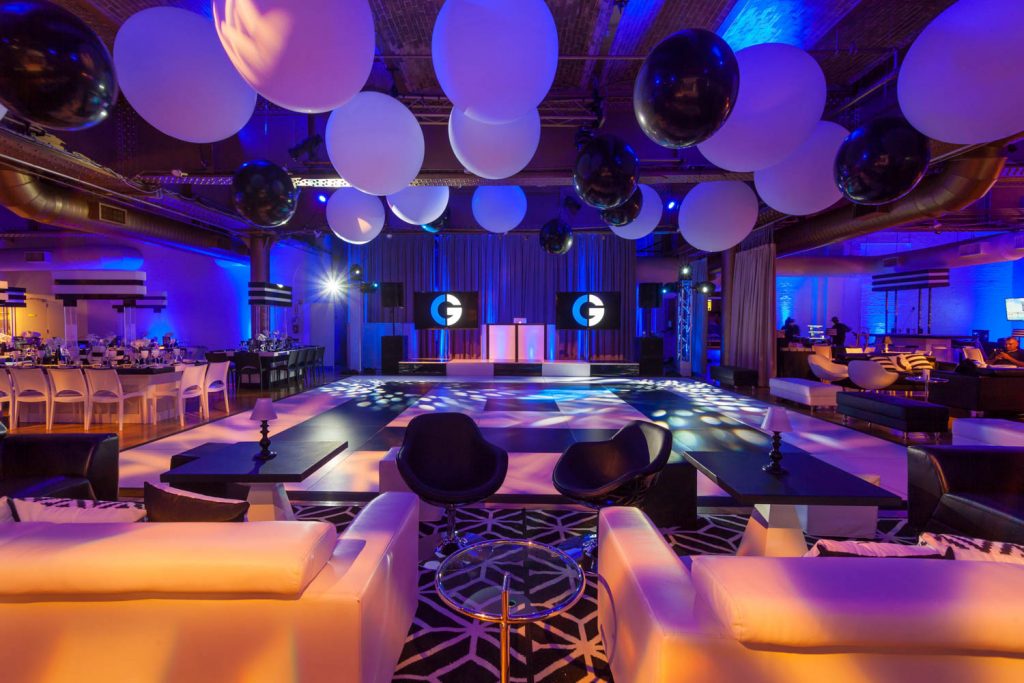 Elegant event space with a dance floor, seating areas, and large overhead balloons in a blue-lit venue.