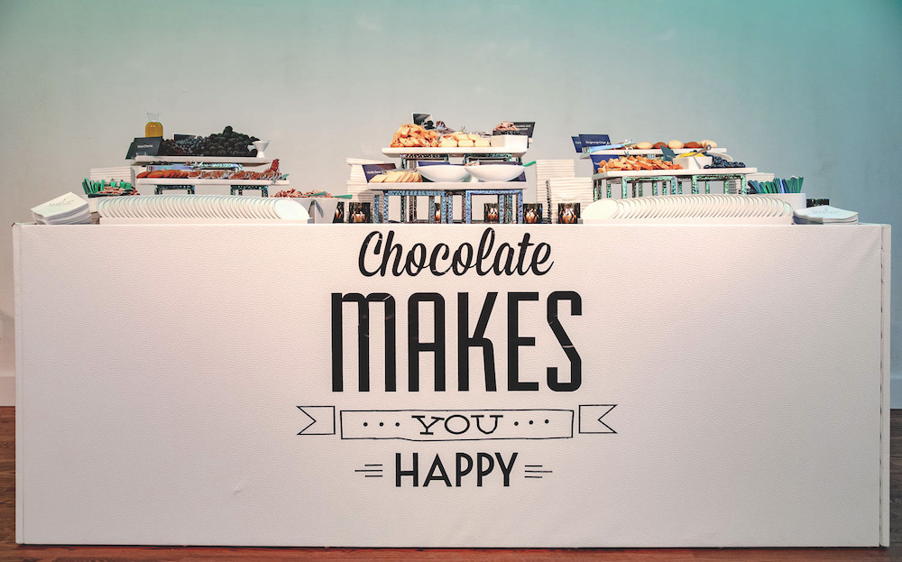 A table with a variety of chocolates and the phrase "chocolate makes ... you ... happy" displayed on its front panel.