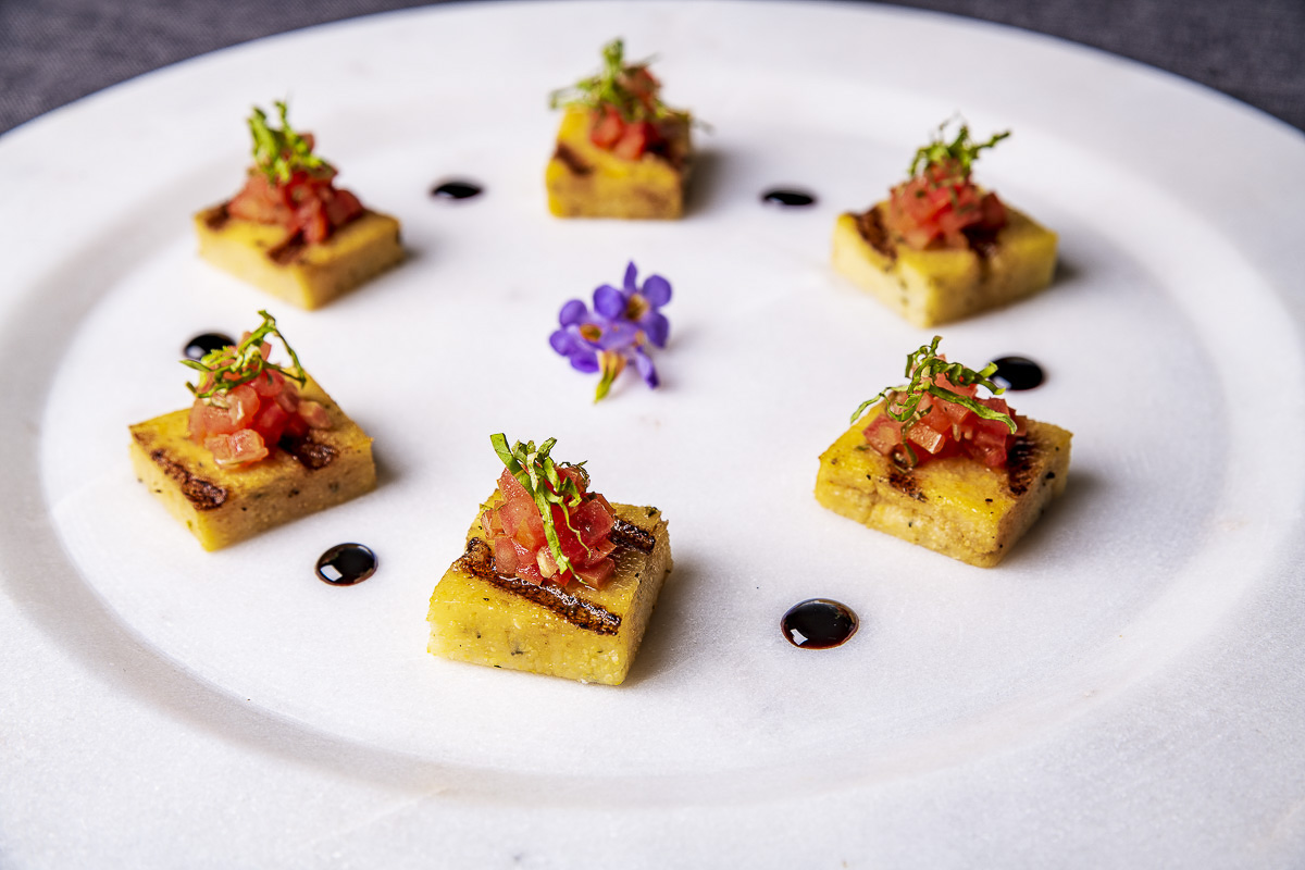 Elegant appetizers: polenta squares topped with tomato concasse and garnished with herbs on a white plate with balsamic reduction.