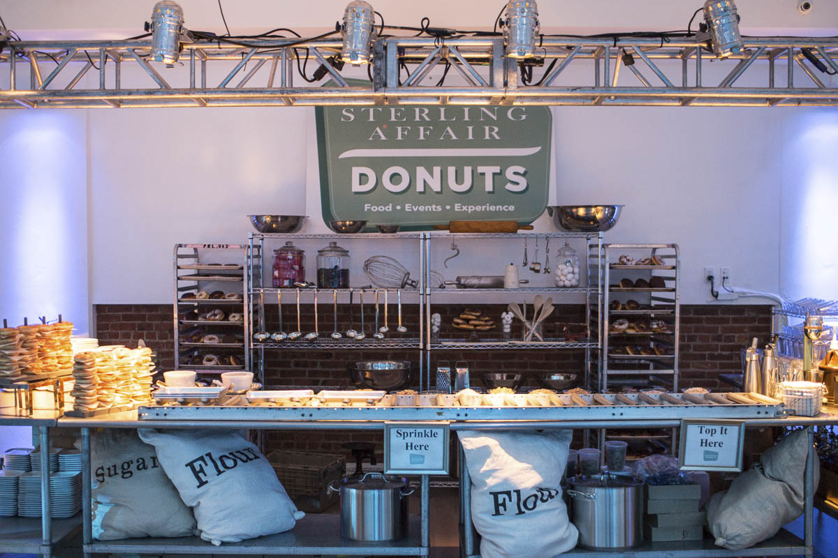 A donut station setup with toppings and ingredients under a "sterling affair donuts" sign.