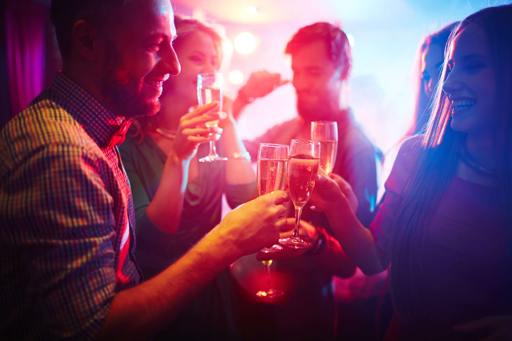 Group of friends toasting with champagne at a party with colorful lighting.