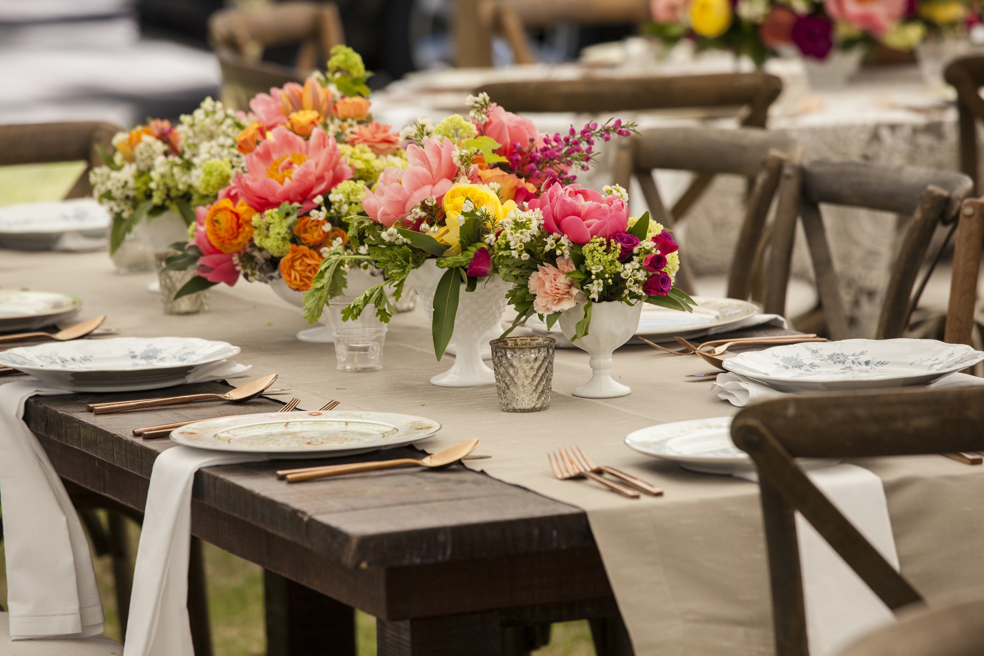 An elegant outdoor table setting with vibrant floral centerpieces and vintage dinnerware.