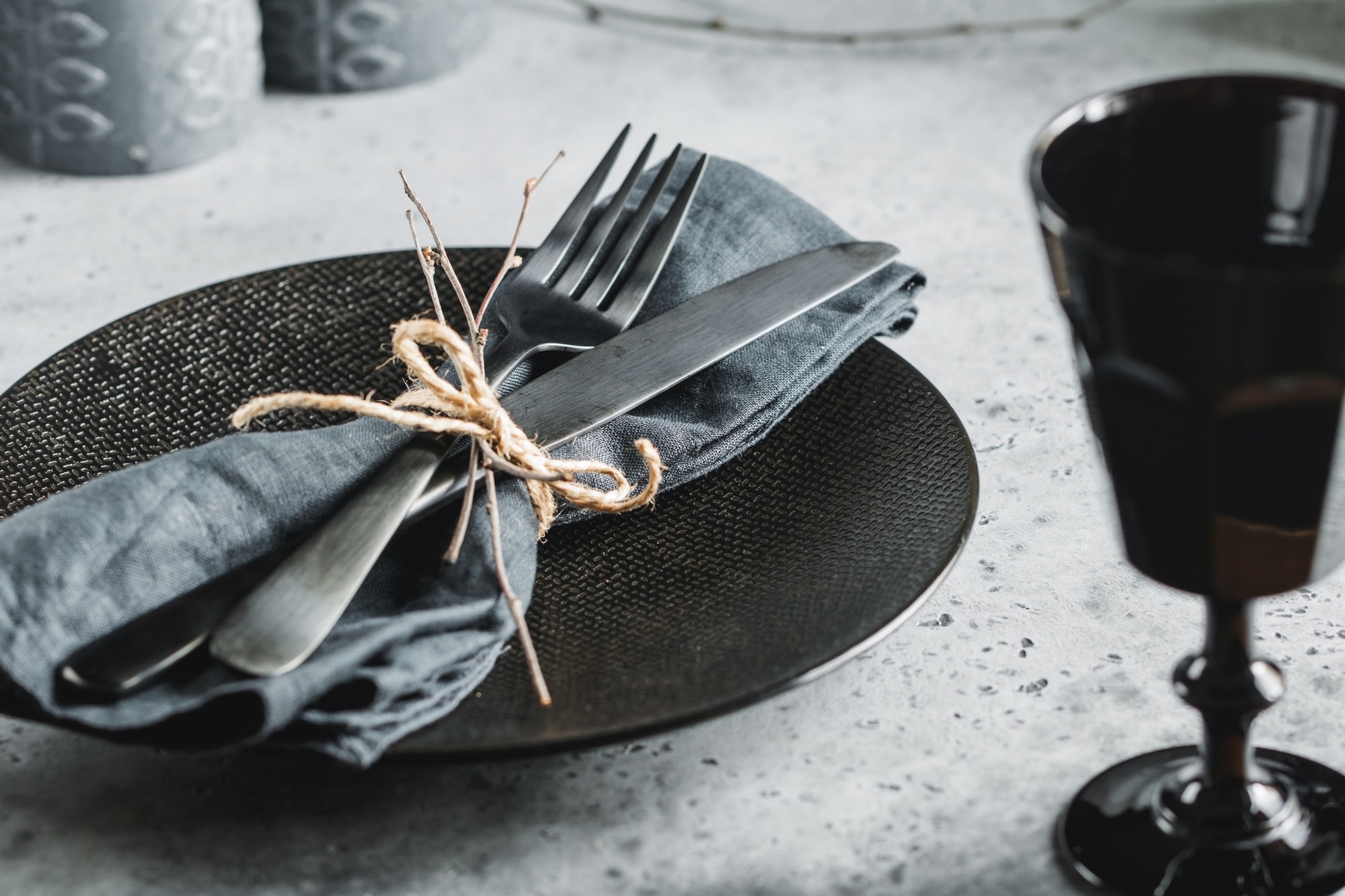 Elegantly set table with black dinnerware and utensils tied with a twine on a cloth napkin.