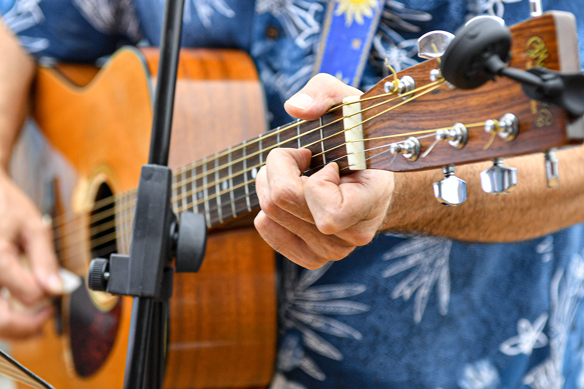 Guitarist playing an acoustic guitar, focusing on hand placement and fretboard.