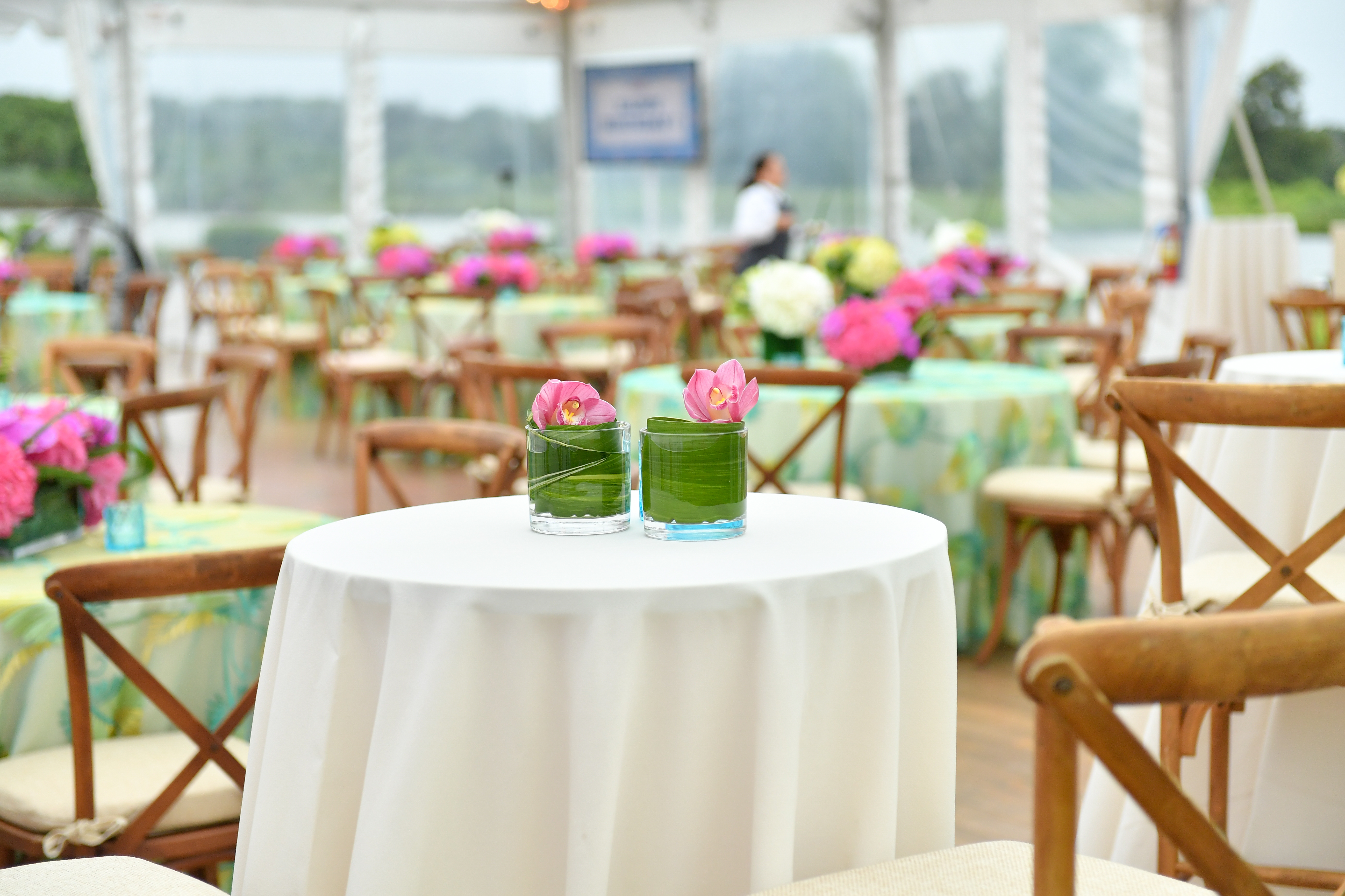 Elegant outdoor event setup with floral centerpieces on white-covered tables and a tent in the background.