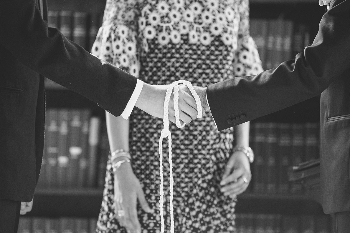 Two individuals holding hands, connected by a white string, symbolizing unity or a ceremony.