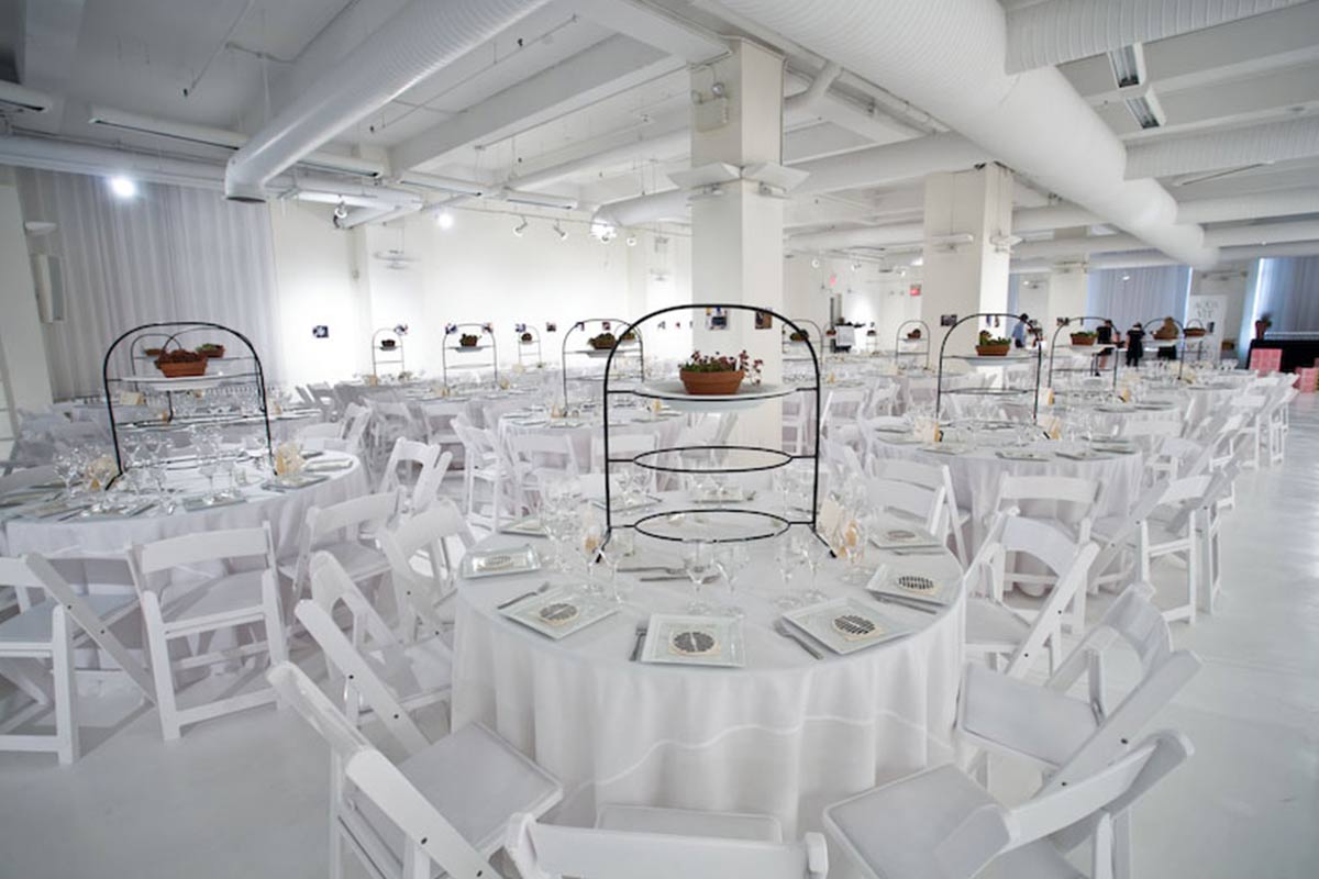 An elegant banquet hall set up for an event with white chairs, table settings, and decorative floral centerpieces.