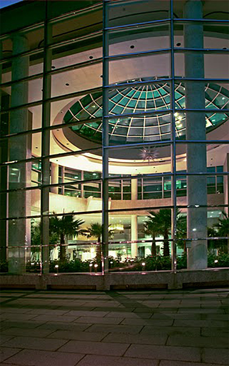 Illuminated modern building facade at night with glass panels and a central dome structure.